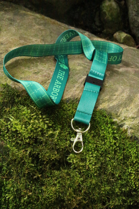 Green lanyard with 'University of Guelph Arboretum' text on one side, and a centimeters ruler on the other side, on a stone with moss. The metal swivel clip and safety breakaway clip are shown.