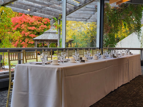 photo of a head table set for dinner in front of the West Lawn windows with the gazebo and trees with fall colours in the background.