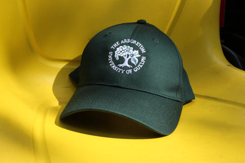 A forest-green ball cap hat, with an embroidered Arboretum tree logo and text "The Arboretum, University of Guelph" on the front. The hat sits on a bright yellow Gator vehicle seat.