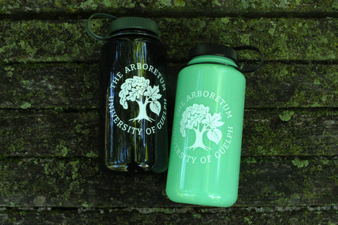 The forest-green and glow-green Nalgene 32oz water bottles, with white Arboretum logos on them, against a mossy wooden bench.